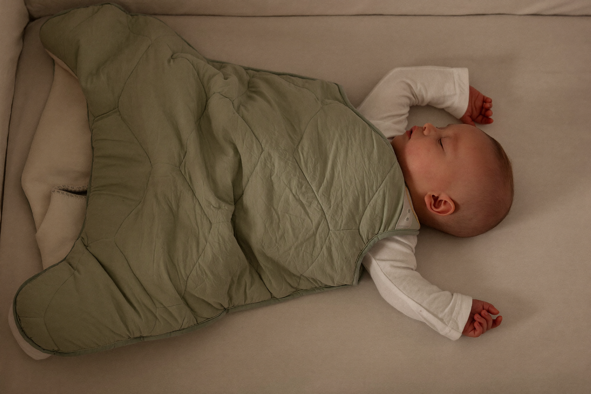 Bébé endormi sur le dos dans son lit, en gigoteuse matelassée vert sauge par-dessus un pyjama en coton Image